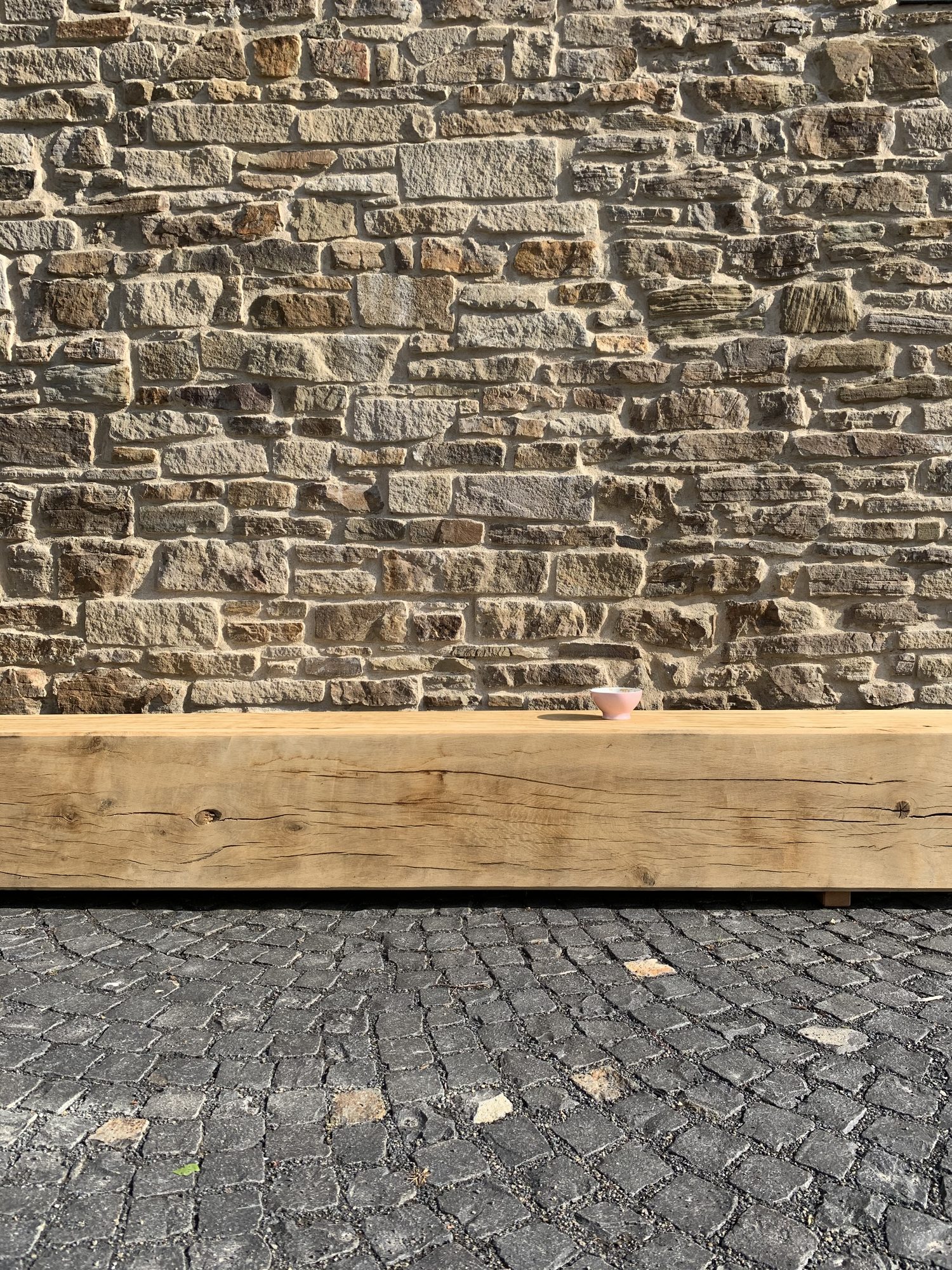 Alte Steinmauer über einer Eichenholzbank mit kleiner Keramikschale